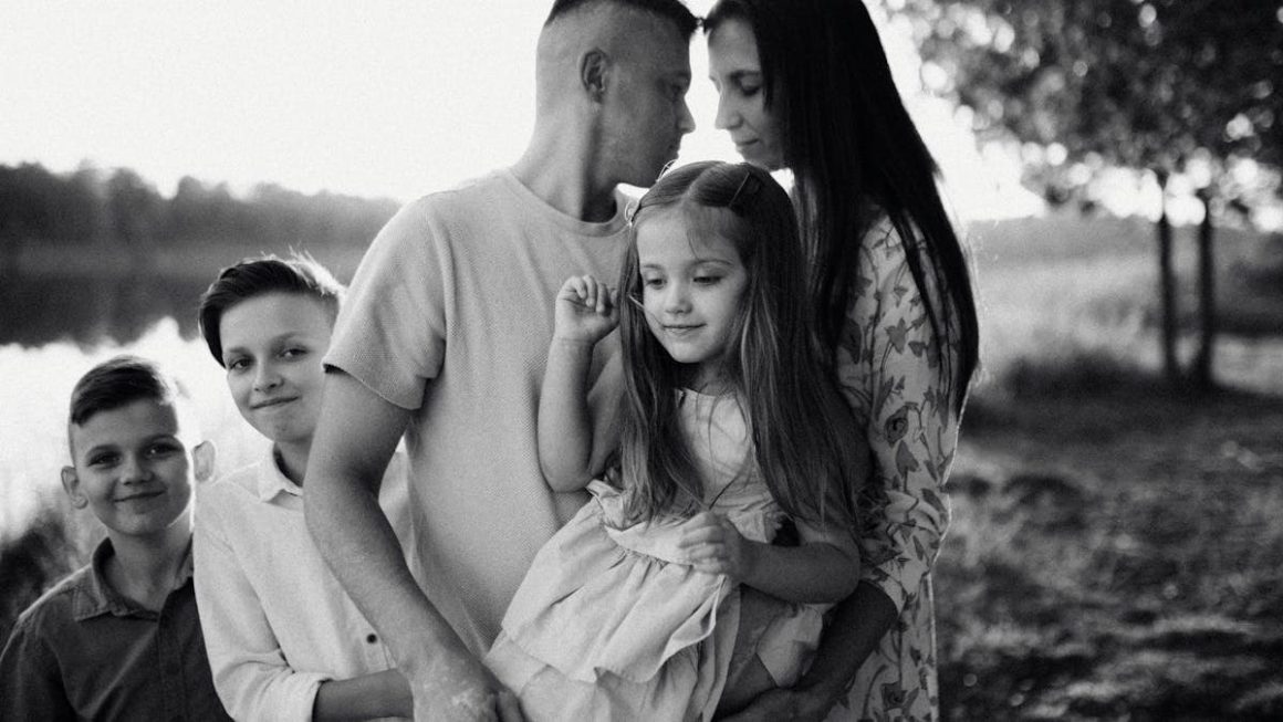 A serene black and white portrait of a family standing by a lake.