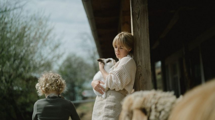 A serene moment captured of a woman cuddling a rabbit outdoors on a farm porch.