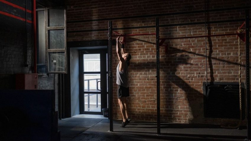 A man exercises on a pull-up bar in an industrial-style gym with brick walls, conveying fitness and dedication.